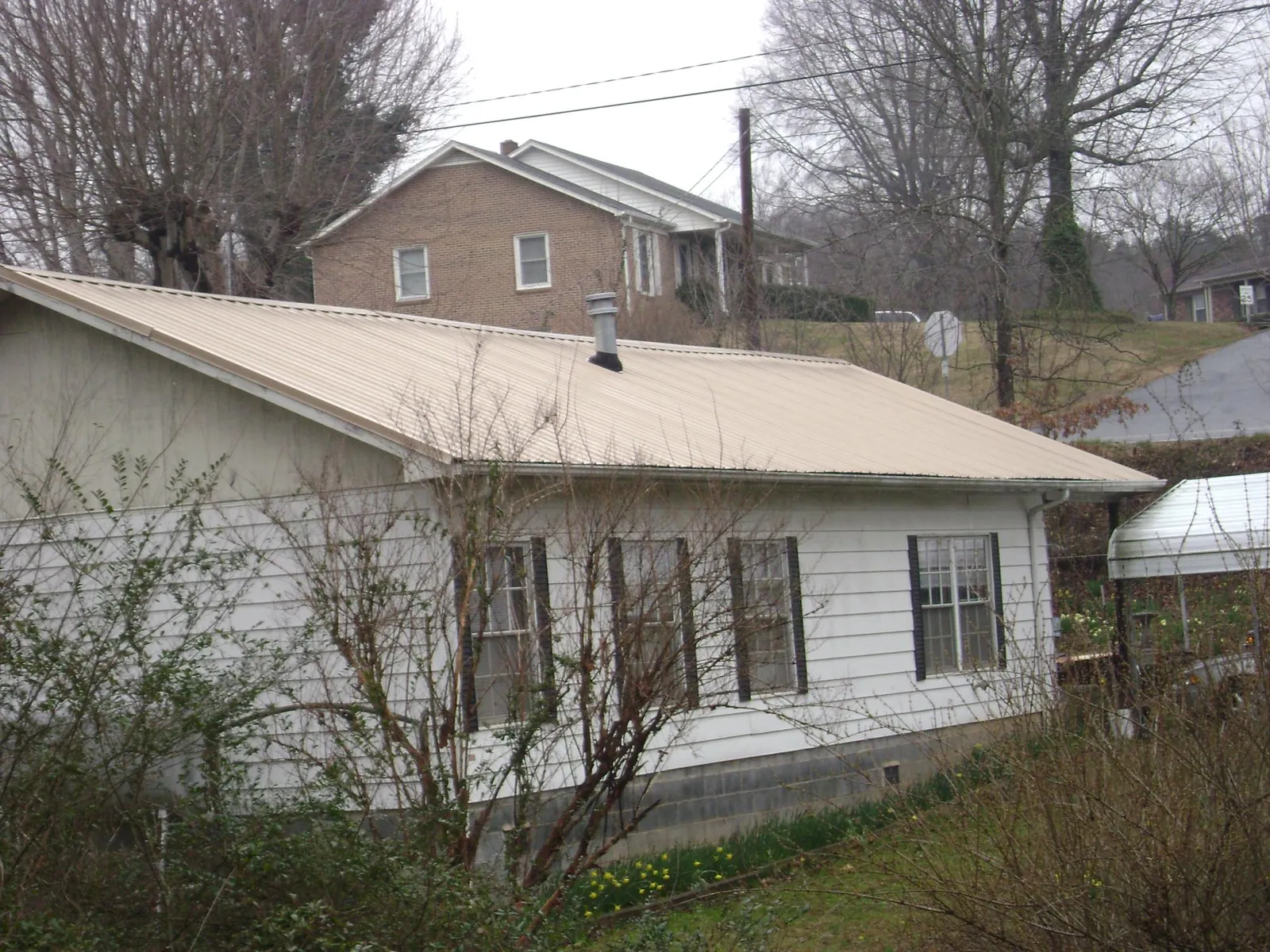 Tan metal roof on a white sided house set into a hillside — Commercial Roofing by Roofing Brothers in Mount Morris